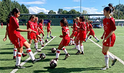 oung girls' soccer team practicing on a synthetic turf field, wearing red uniforms.